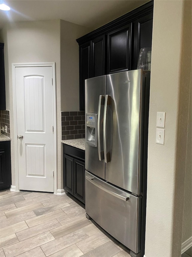 kitchen with stainless steel fridge with ice dispenser, dark cabinets, backsplash, and light wood-type flooring