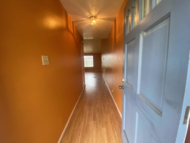 corridor featuring a textured ceiling, baseboards, and wood finished floors