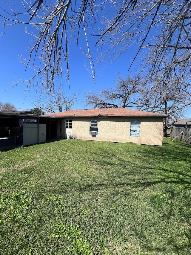 rear view of house featuring a lawn, fence, and stucco siding