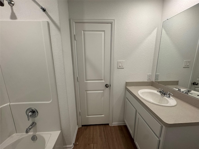 bathroom featuring shower / bathtub combination, a textured wall, vanity, wood finished floors, and baseboards