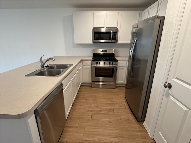 kitchen featuring appliances with stainless steel finishes, a peninsula, light wood-style floors, white cabinetry, and a sink