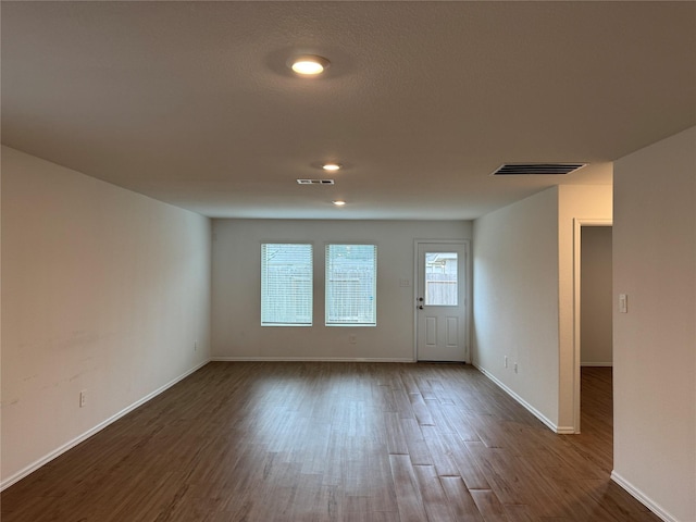 spare room with dark wood-type flooring, visible vents, and baseboards