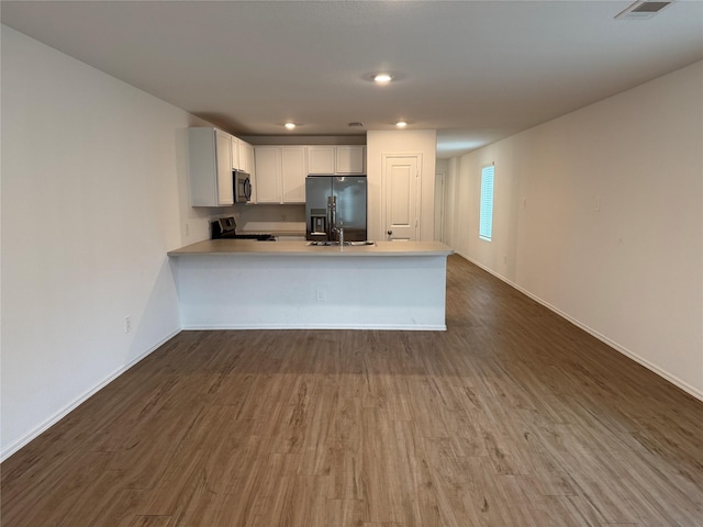 kitchen featuring dark wood-style flooring, light countertops, appliances with stainless steel finishes, white cabinetry, and a peninsula