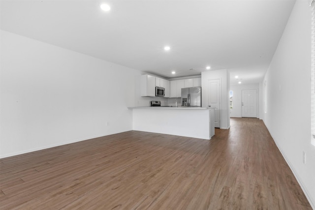 17594 Longwood Trace Ln, New Caney, TX 77357 - kitchen featuring appliances with stainless steel finishes, a peninsula, light wood finished floors, open floor plan, and white cabinetry