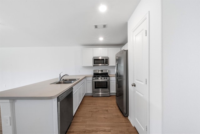 17594 Longwood Trace Ln, New Caney, TX 77357 - kitchen with stainless steel appliances, a sink, a peninsula, wood finished floors, and white cabinets
