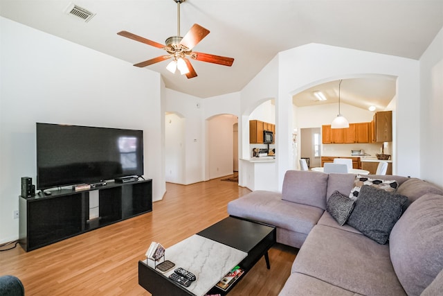 living area featuring visible vents, arched walkways, a ceiling fan, lofted ceiling, and light wood-style floors