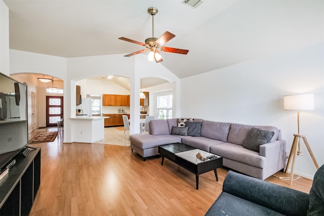 living room featuring lofted ceiling, ceiling fan, arched walkways, light wood-style flooring, and visible vents