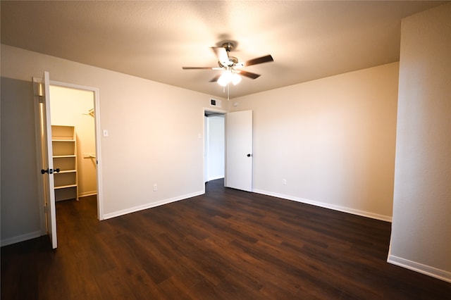 unfurnished bedroom featuring dark wood-type flooring, visible vents, a spacious closet, and baseboards