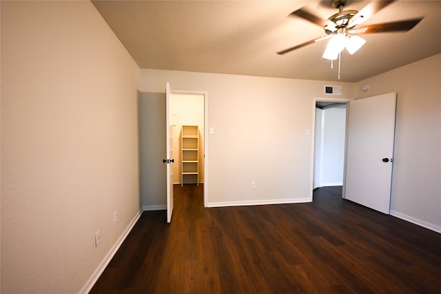 unfurnished bedroom with baseboards, visible vents, a walk in closet, and dark wood-style flooring