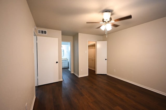 unfurnished bedroom with dark wood-style flooring, visible vents, baseboards, a closet, and a walk in closet