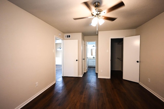 unfurnished bedroom with a walk in closet, baseboards, visible vents, and dark wood finished floors