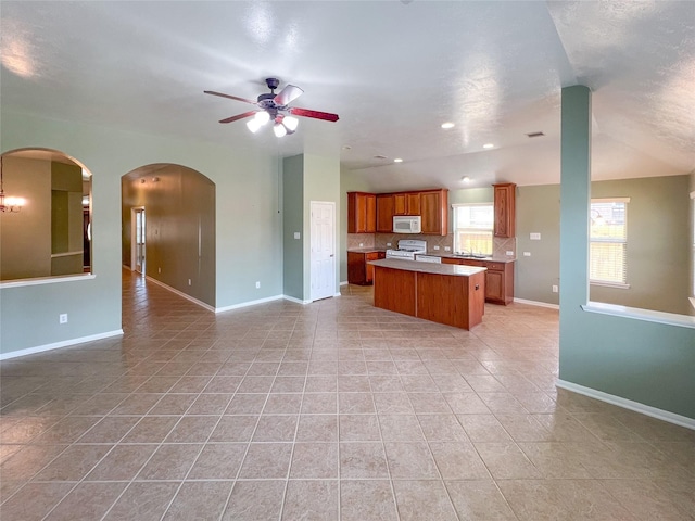 kitchen featuring light tile patterned flooring, white appliances, a kitchen island, open floor plan, and brown cabinetry