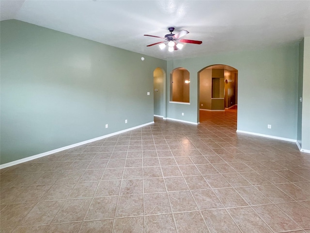 unfurnished room featuring arched walkways, lofted ceiling, light tile patterned flooring, a ceiling fan, and baseboards