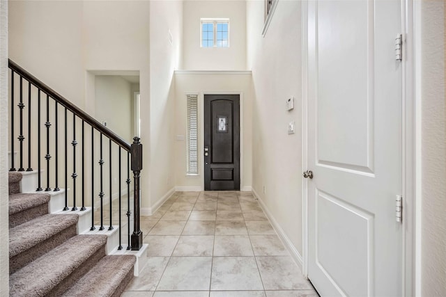 entryway with a towering ceiling, light tile patterned floors, stairs, and baseboards