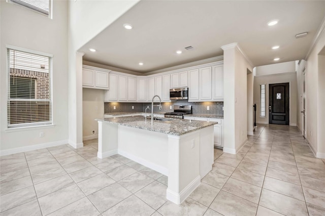 kitchen featuring light tile patterned flooring, a sink, appliances with stainless steel finishes, decorative backsplash, and an island with sink