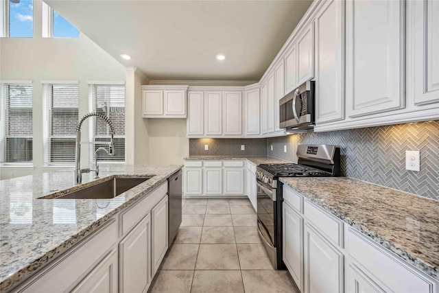 kitchen with appliances with stainless steel finishes, light tile patterned flooring, a sink, and white cabinets