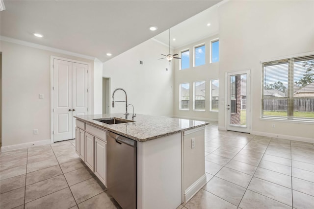 kitchen with light stone counters, a center island with sink, light tile patterned flooring, a sink, and dishwasher