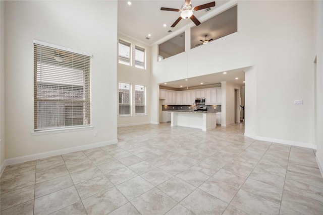 unfurnished living room featuring light tile patterned floors, recessed lighting, a towering ceiling, a ceiling fan, and baseboards