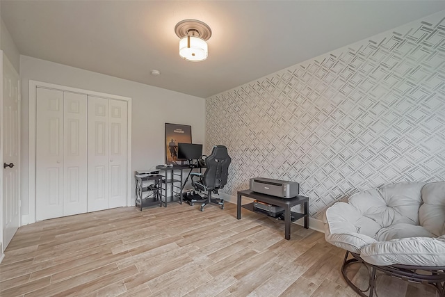 office area with light wood-style floors, an accent wall, and wallpapered walls