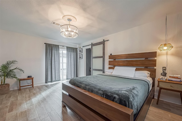 bedroom with a notable chandelier, visible vents, a barn door, wood finished floors, and baseboards