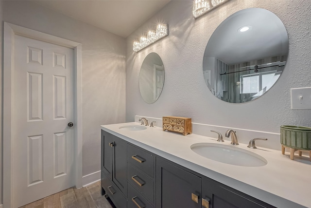 full bathroom featuring double vanity, a textured wall, a sink, and wood finished floors