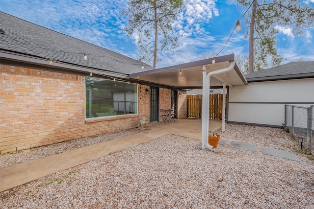 rear view of house featuring roof with shingles, fence, brick siding, and a patio