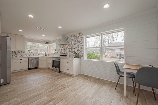 kitchen with a sink, exhaust hood, visible vents, appliances with stainless steel finishes, and a wealth of natural light