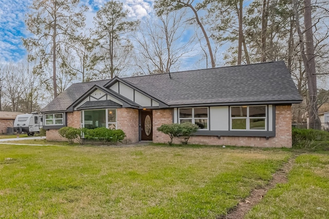 view of front facade with brick siding, roof with shingles, and a front yard