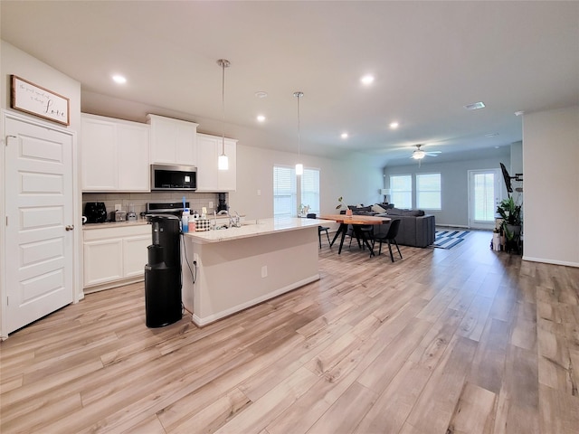 kitchen featuring light wood-type flooring, tasteful backsplash, stainless steel microwave, and open floor plan