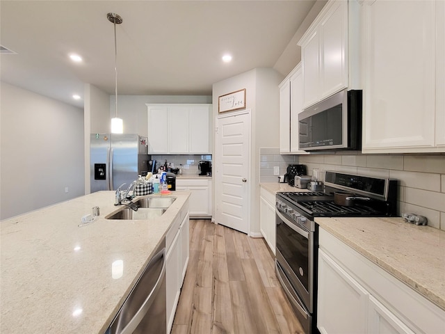 kitchen featuring light wood finished floors, white cabinets, decorative backsplash, appliances with stainless steel finishes, and a sink