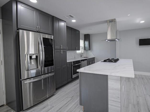 kitchen with range hood, stainless steel appliances, visible vents, a kitchen island, and light wood-type flooring