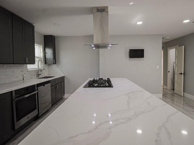 kitchen featuring island range hood, dark cabinets, a sink, stainless steel appliances, and backsplash