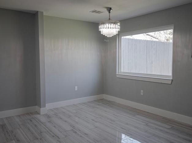 unfurnished room with baseboards, visible vents, a notable chandelier, and wood finished floors