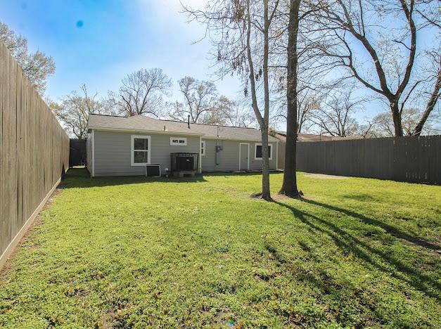 back of house featuring a fenced backyard, a lawn, and central AC