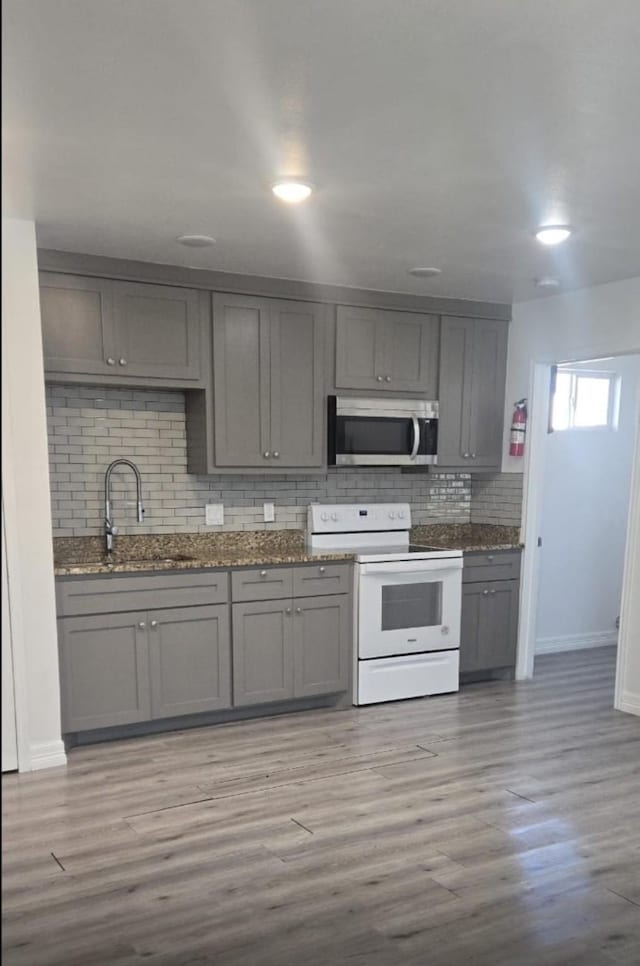 kitchen with light wood-style floors, stainless steel microwave, gray cabinetry, and white electric range oven