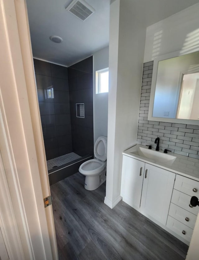 bathroom featuring visible vents, backsplash, toilet, a shower stall, and wood finished floors