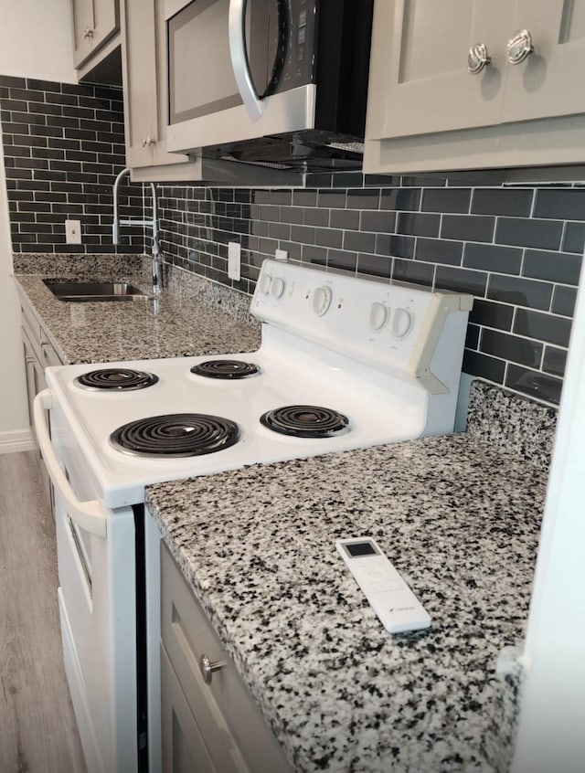 kitchen featuring a sink, wood finished floors, backsplash, white range with electric stovetop, and stainless steel microwave