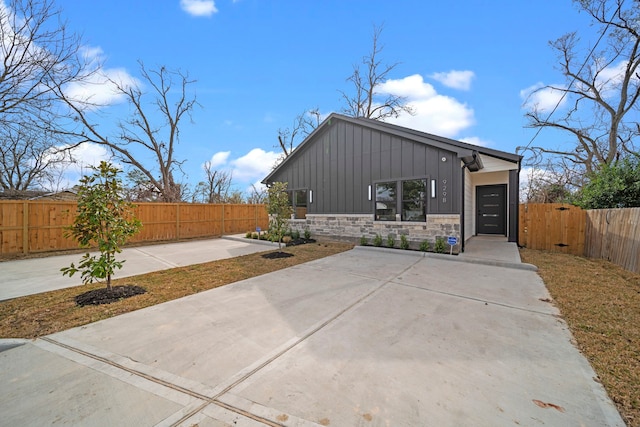 view of front facade featuring board and batten siding, stone siding, fence, and a patio