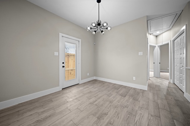 empty room featuring attic access, light wood-type flooring, baseboards, and an inviting chandelier