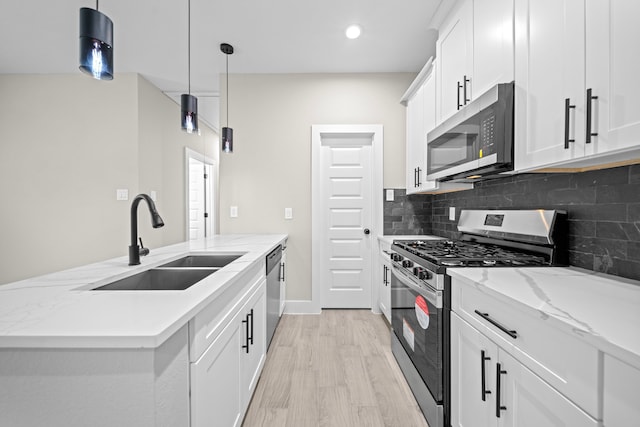 kitchen featuring stainless steel appliances, a sink, white cabinets, light wood-style floors, and backsplash