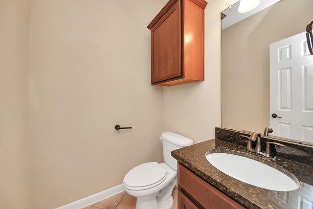 half bathroom with toilet, vanity, baseboards, and tile patterned floors