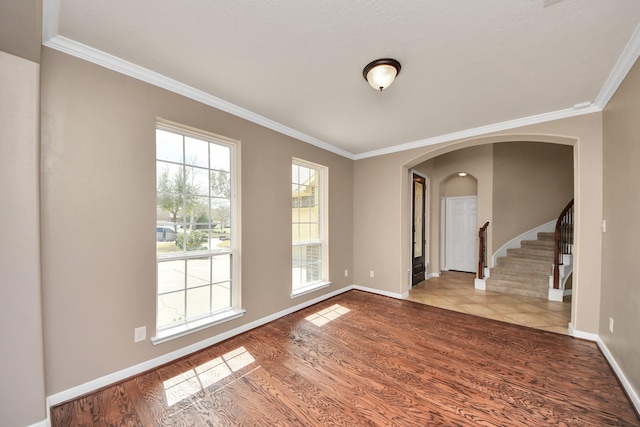 unfurnished room featuring arched walkways, wood finished floors, baseboards, stairs, and crown molding