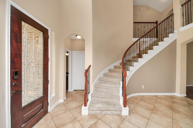 foyer entrance featuring baseboards, high vaulted ceiling, arched walkways, and tile patterned floors