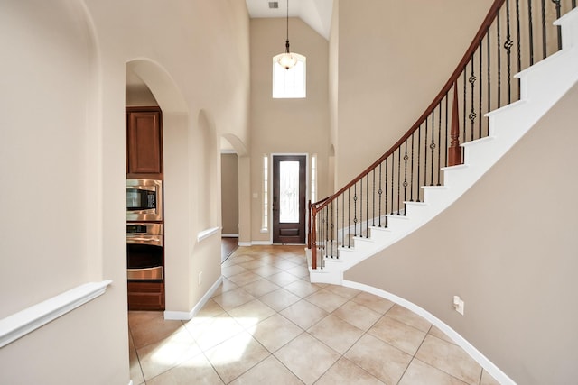 foyer entrance with a towering ceiling, light tile patterned floors, baseboards, and a wealth of natural light