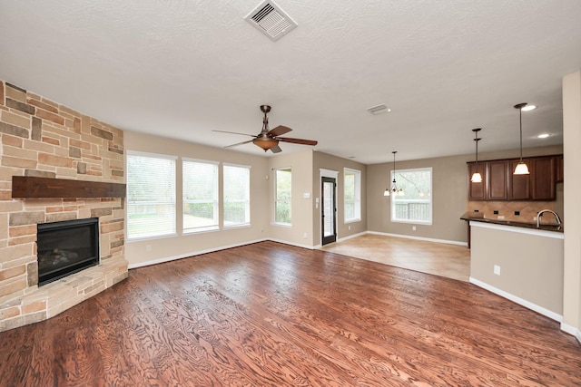 unfurnished living room featuring visible vents, wood finished floors, a stone fireplace, a sink, and ceiling fan with notable chandelier