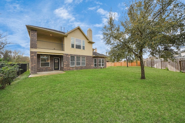 back of property with a fenced backyard, a balcony, brick siding, a lawn, and a chimney