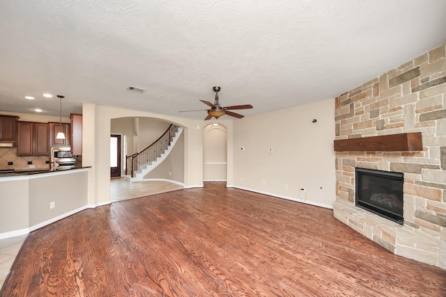 unfurnished living room featuring arched walkways, a fireplace, wood finished floors, visible vents, and stairs