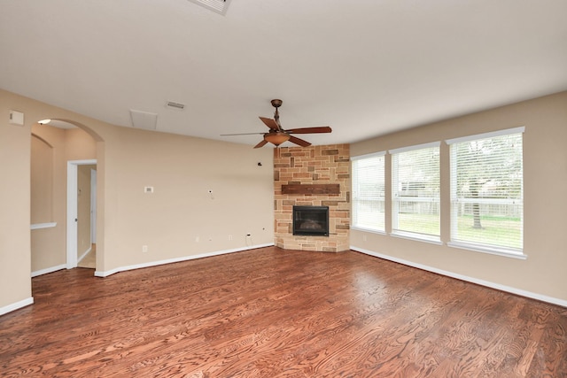 unfurnished living room featuring baseboards, arched walkways, a ceiling fan, wood finished floors, and a stone fireplace