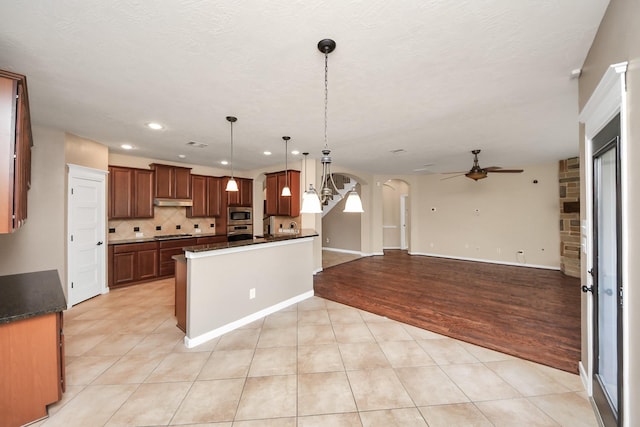 kitchen featuring dark countertops, open floor plan, arched walkways, and decorative backsplash