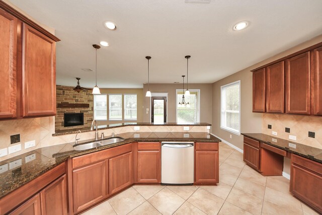 kitchen with dishwasher, dark stone counters, a sink, and brown cabinetry